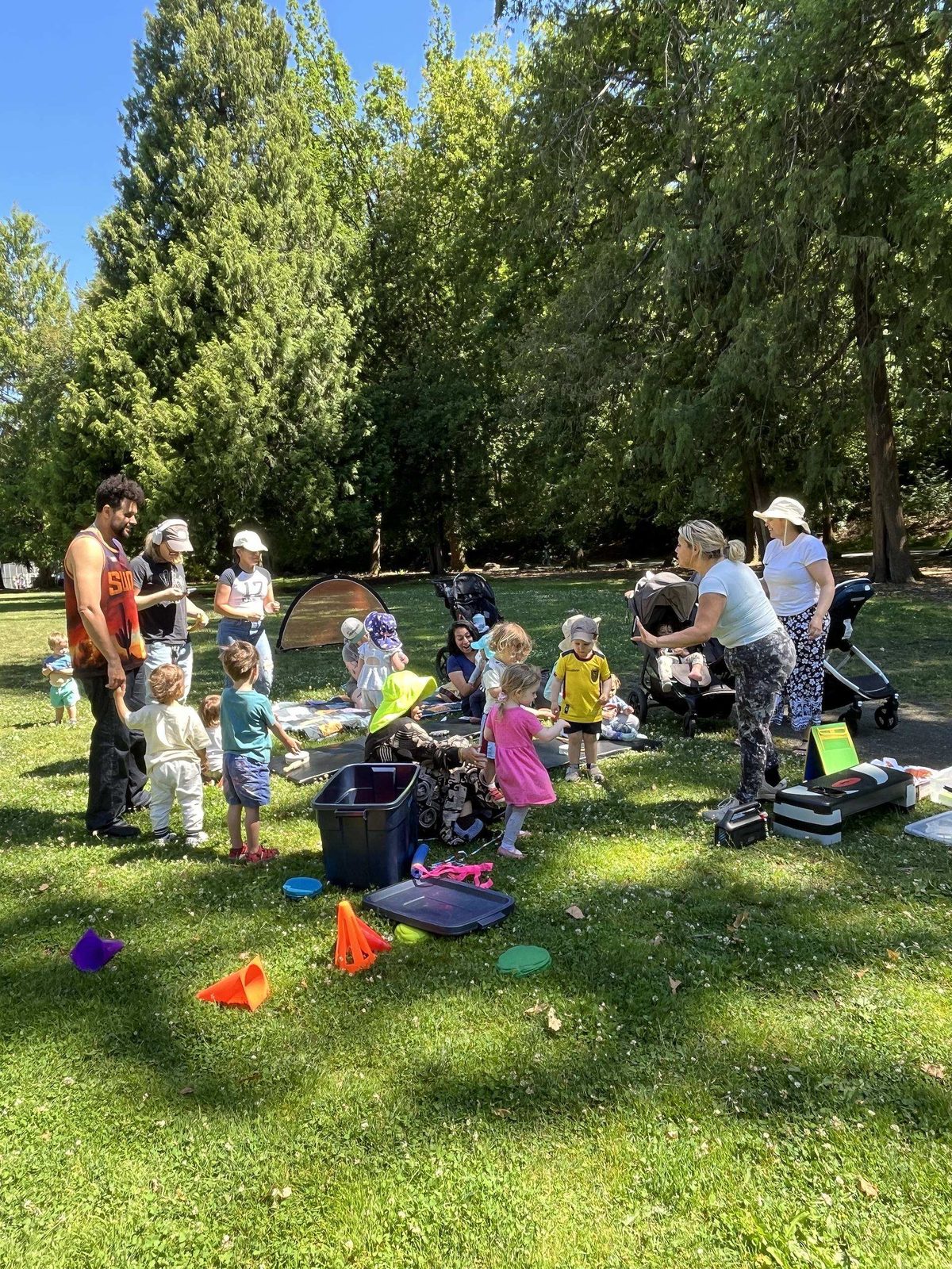 Rec N’ The Streets staff and families with young children around recreation equipment on the grass at Mount Baker Park